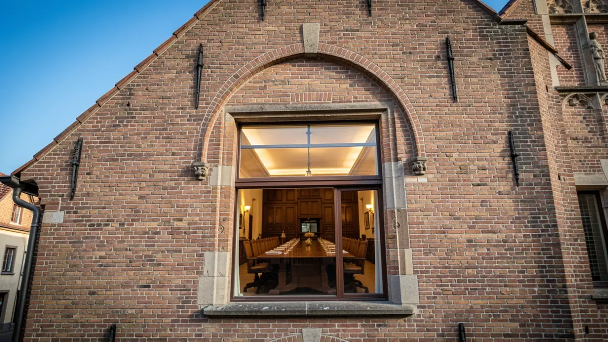 De gevel van een Vlaams gemeentehuis met een raadzaal, traditionele baksteenarchitectuur onder een blauwe hemel.