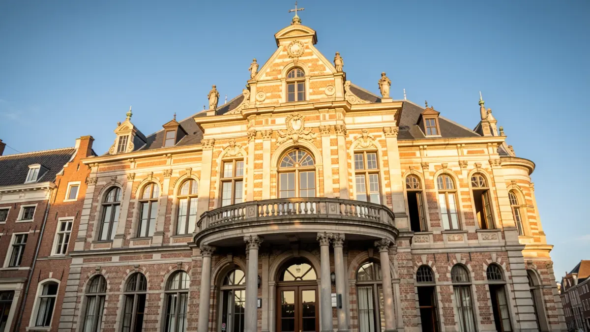 Historische gevel van een Vlaams gemeentehuis met een balkon, in de namiddagzon.