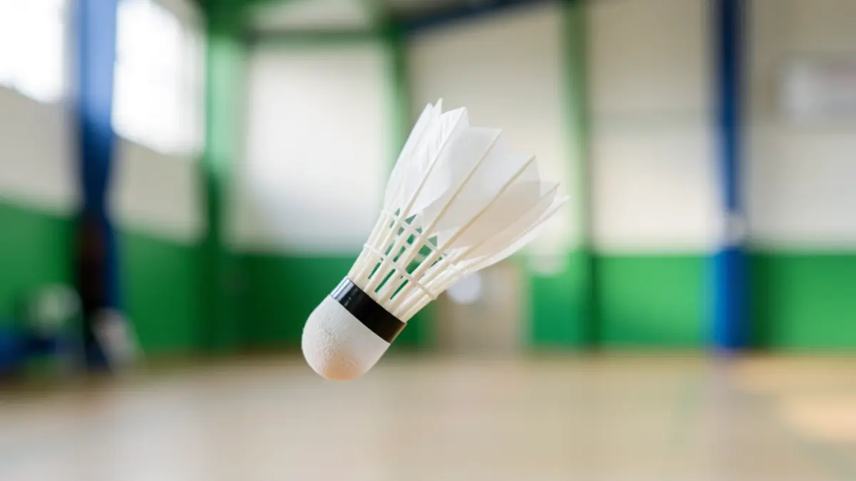 Close-up van een badmintonshuttle in de lucht in een sportzaal.