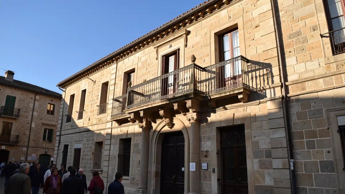 Generic image of a traditional stone town hall facade with an ornate balcony and iron railings, warm afternoon sunlight casting shadows on the sandstone walls, blue sky, in documentary photography style.