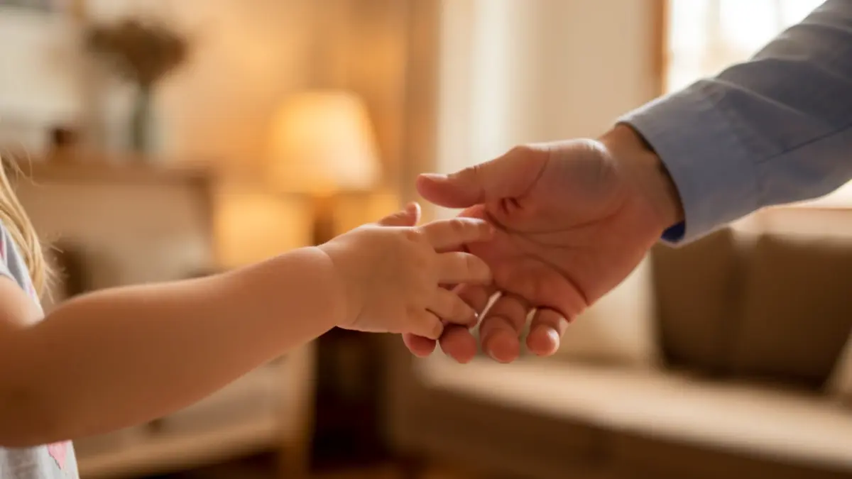 A child's hand reaching towards a blurred adult hand in a warm, softly lit room, symbolizing support and guidance.