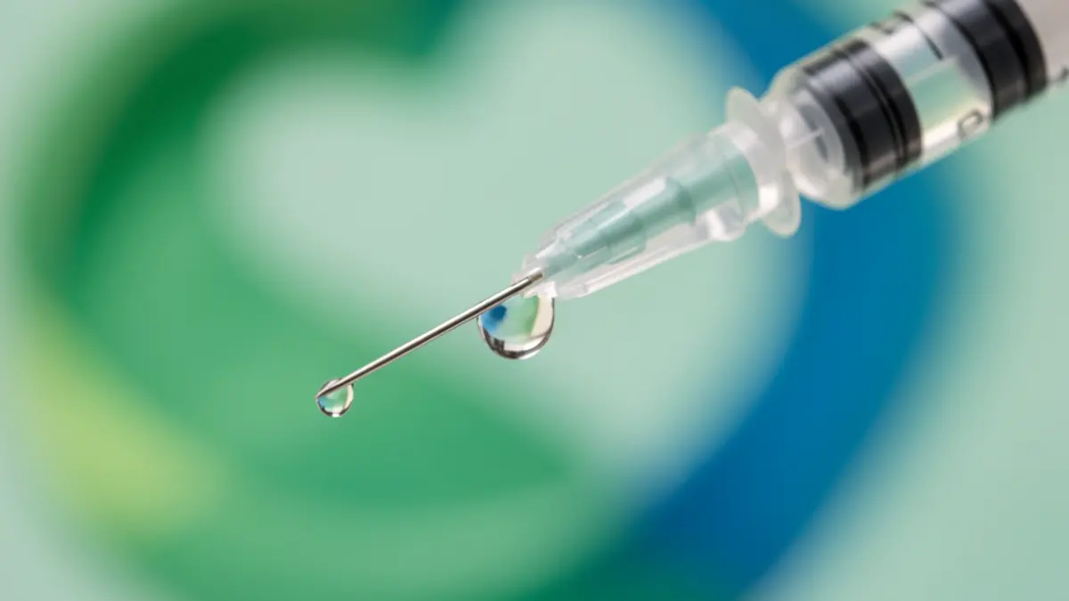 Generic image of a medical syringe with a drop of liquid, against a blurred background symbolizing health and protection.